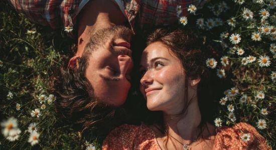 Una pareja reconquistada acostada en un campo de hierba y flores, mirándose mutuamente con ternura