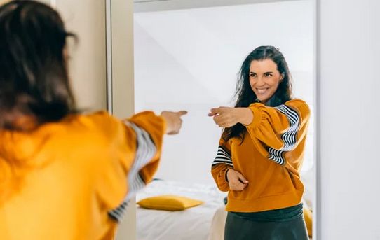 Persona frente al espejo, señalándose con seguridad y empoderamiento, simbolizando la liberación de la codependencia emocional.